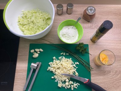 Sýr nakrájený na kostičky na zeleném prkénku s nožem a lisem na česnek