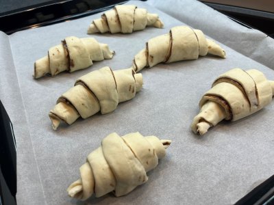 Neupečené croissanty z listového těsta na plechu vyloženém pečicím papírem