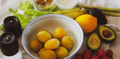 Na stole položeny uvařené brambory v míse, rozpůlené avokádo, ředkvičky, citron, řapíkatý celer, sůl, pepř