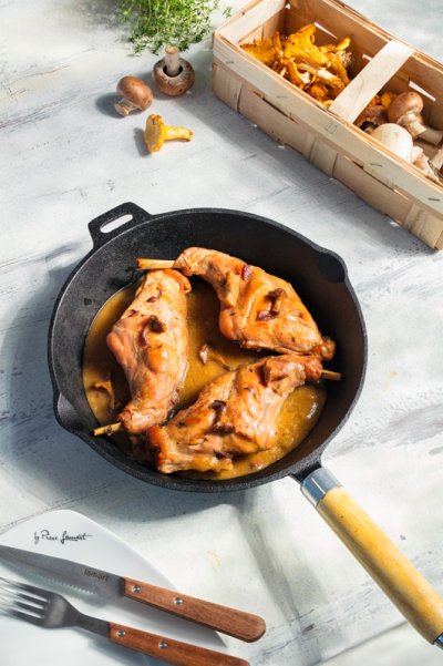 Králičí stehno na houbách na pánvi na světlém stole