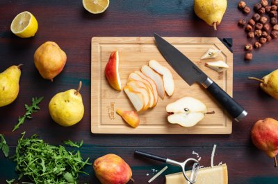 Nákrájená hruška na dřevěném prkénku, vedle rukola a oříšky