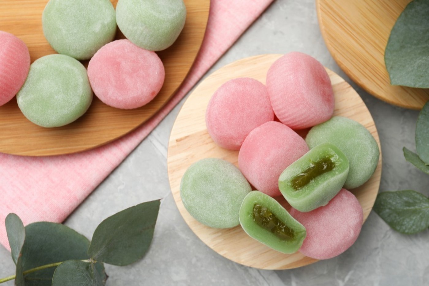 Japonské mochi koláčky zelené a růžové, servírované na prkénku, na šedém stole