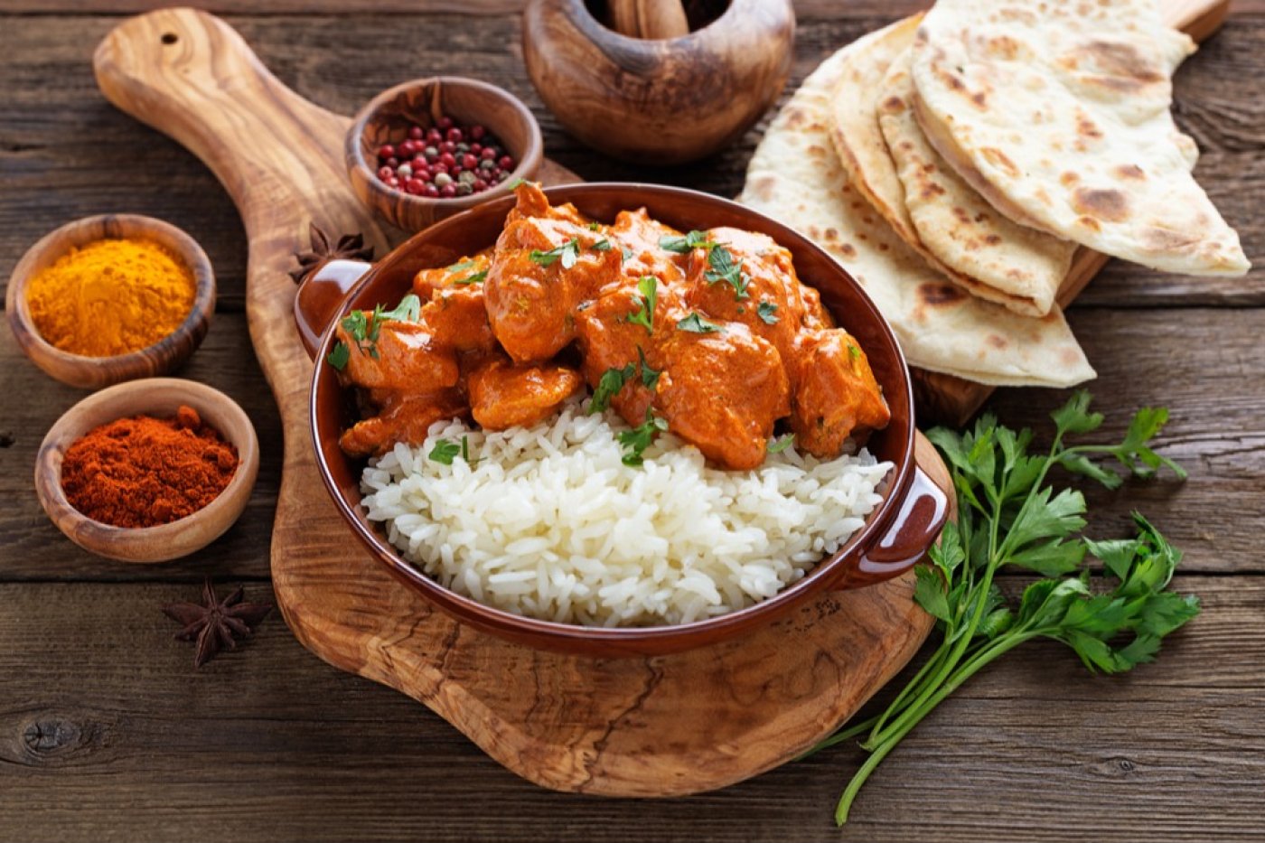 butter chicken s rýží servírované v hnědé míse ležící na dřevěném prkénku