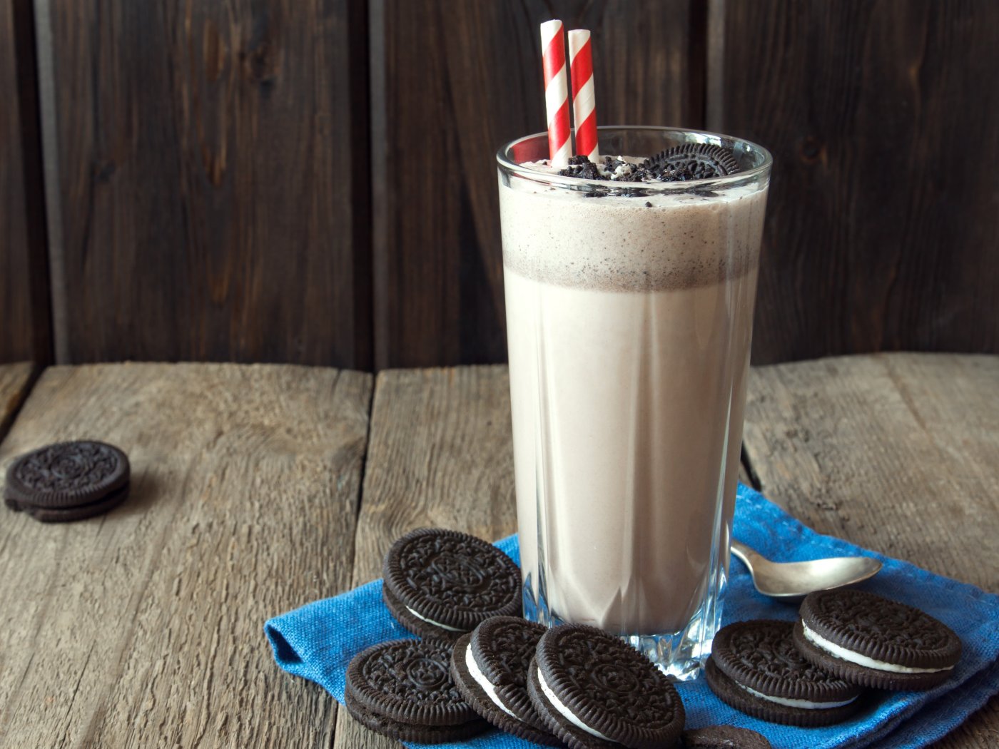 Oreo milkshake ve vysoké sklenici se dvěmi červeno-bílými slámkami a kousky sušenek