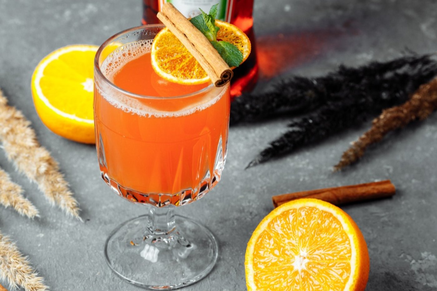 Horký Aperol Spritz ve sklenici na stopce, ozdobený tyčinkou skořice, pomerančem a mátou