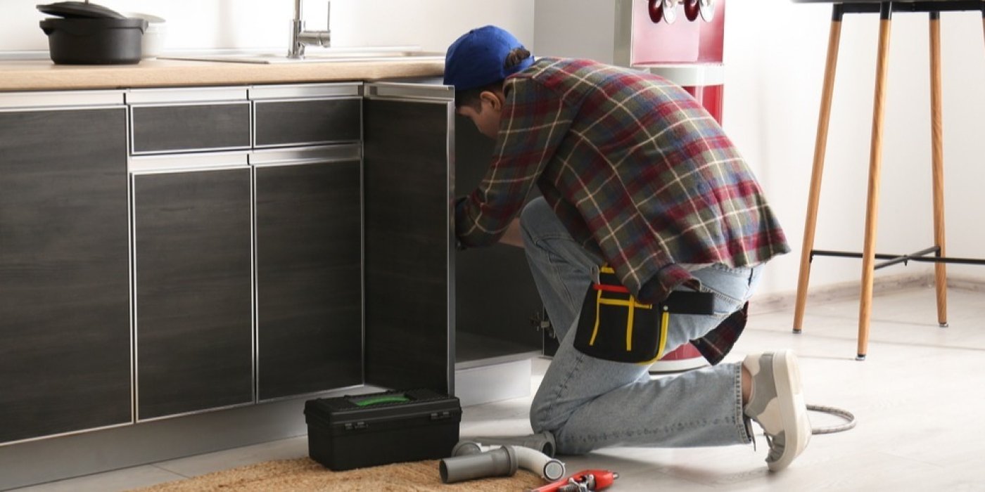 Muž klečí u linky a opravuje odtok dřezu