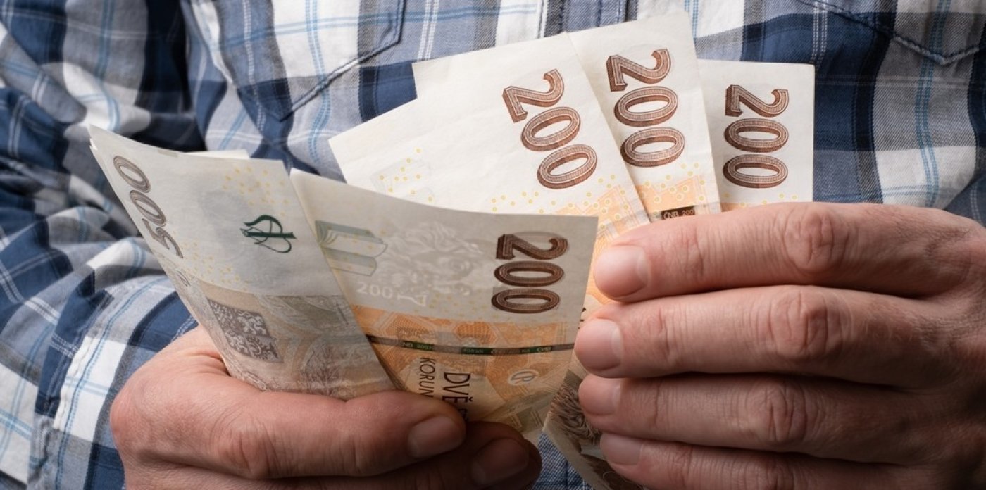 Člověk drží české bankovky v ruce