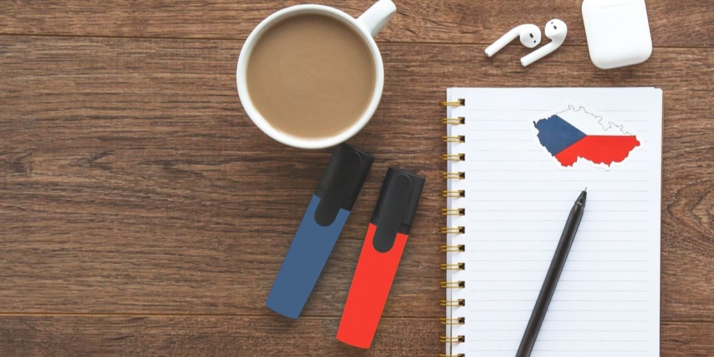 Stůl, na něm zápisník s mapou, kávou, sluchátky i zvýrazňovači