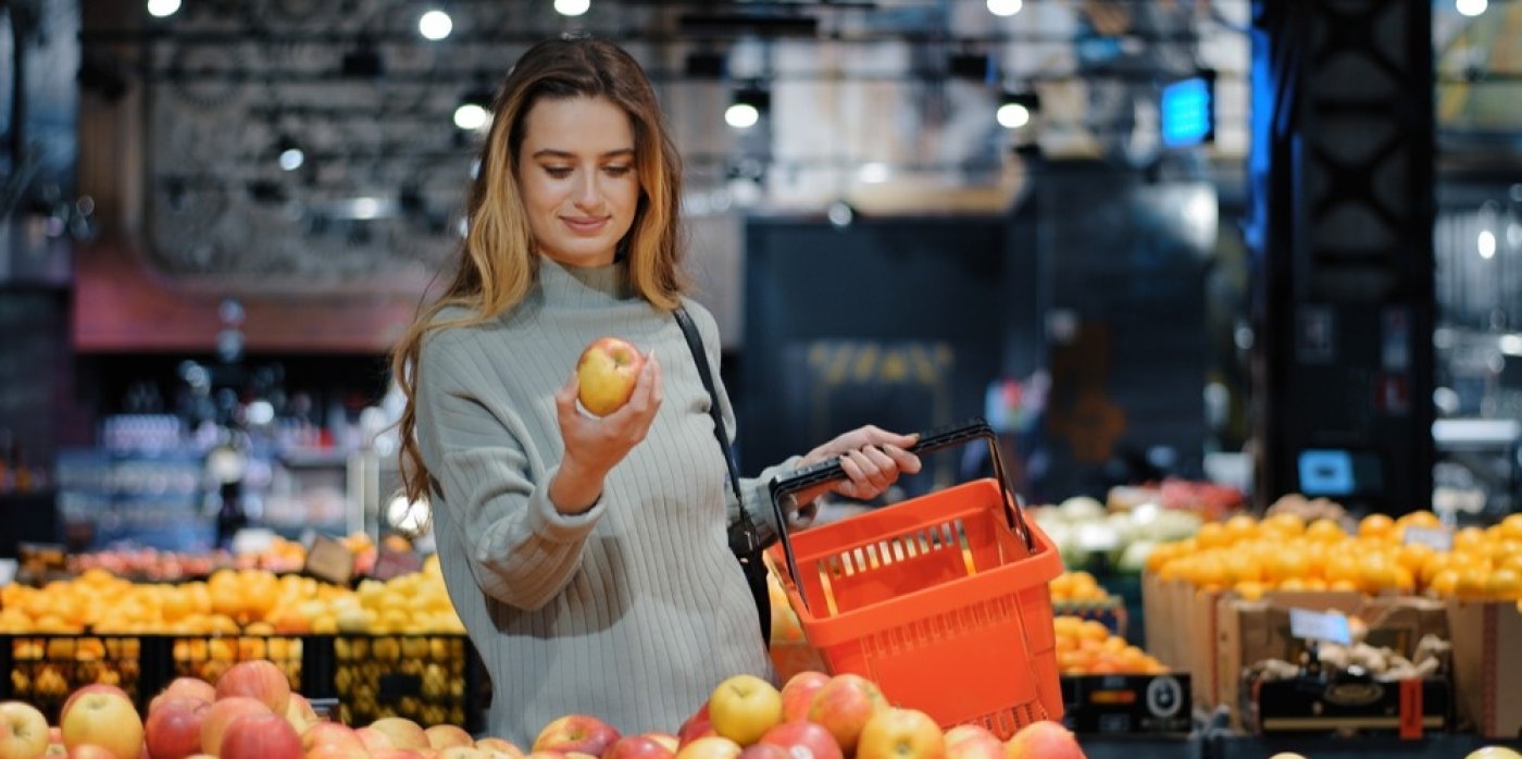 Žena se dívá na jablko v supermarketu